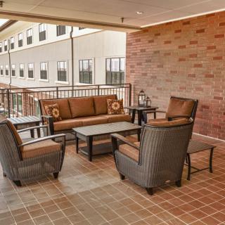 A cozy outdoor patio with a wicker furniture set, including chairs, a sofa, and a coffee table, against a brick wall backdrop.