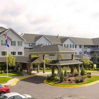 A large residential building with a landscaped entrance and driveway, featuring flags in the foreground.