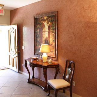 A warmly lit entryway featuring a wooden table with a lamp, a chair, and a decorative painting on the wall.
