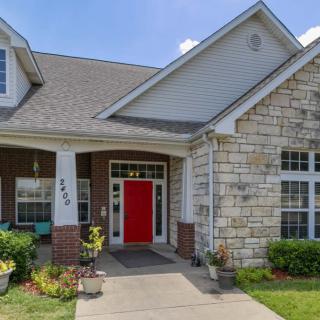 A charming house with a red front door and brick exterior, surrounded by a well-maintained garden.