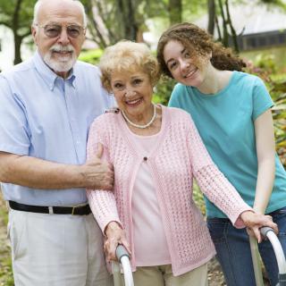 Elderly woman with family members supporting her during a walk outdoors.