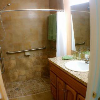 A small bathroom featuring a walk-in shower with a curtain, a sink with a wooden vanity, and tiled walls and floor.