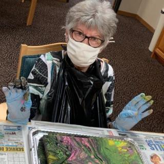 A person engaged in creating abstract art while wearing a mask and gloves.