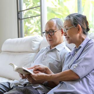 An elderly couple enjoys reading together at home.