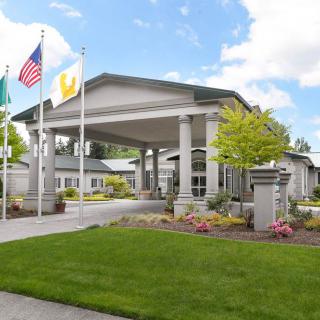A well-maintained building entrance with flags, surrounded by a landscaped lawn under a partly cloudy sky.