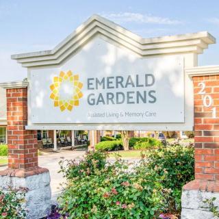 Entrance sign for Emerald Gardens surrounded by greenery and brick pillars.