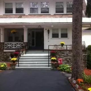 A welcoming house entrance with steps leading up to a porch, surrounded by colorful flowers and trees.