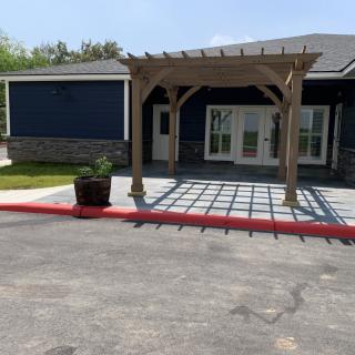 A building entrance with a wooden pergola and paved area.