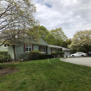 A suburban house with a well-maintained lawn and driveway, surrounded by trees.