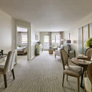 A modern apartment interior with a living and dining area, featuring elegant furniture and a carpeted floor.