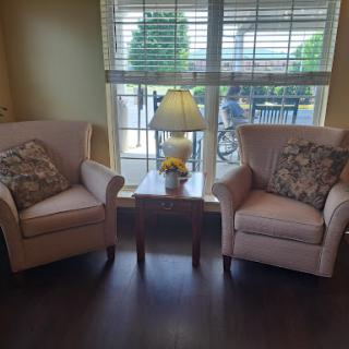 A cozy living room setup featuring two plush chairs, a small table with a lamp, and natural light streaming in through the window.