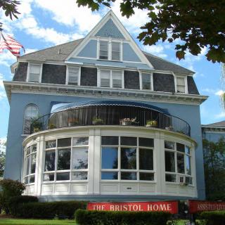 A large Victorian-style blue house with a rounded windowed section and an American flag flying from the roof.