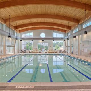 A spacious indoor swimming pool with multiple lanes, featuring a wooden ceiling and large windows.