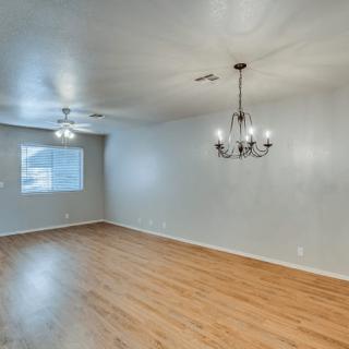 An empty room with wooden flooring, featuring a chandelier and a window with curtains.