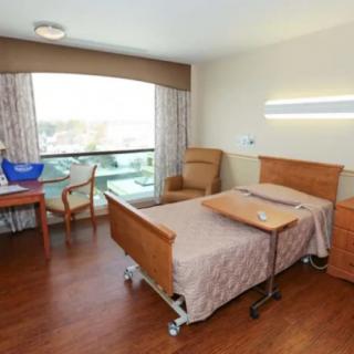 A clean and organized hospital room with a single bed, a chair, and a window providing natural light.