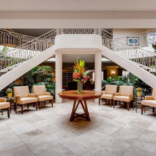 A beautifully designed lobby featuring a central table with flowers, surrounded by chairs and a grand staircase.