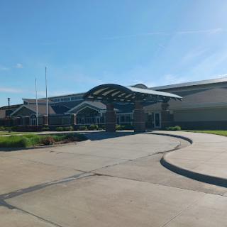 A modern building with a curved roof and landscaped entrance, set in sunny weather.