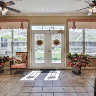 A bright living room with large windows and glass doors, featuring potted plants and comfortable seating.