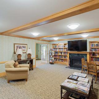 A cozy library room with bookshelves, a seating area, fireplace, and television.