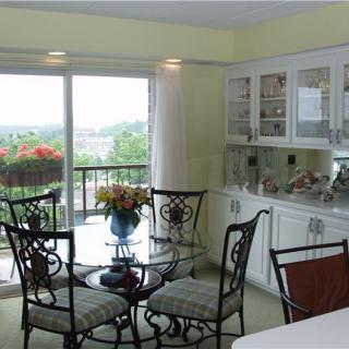 A cozy dining room with a glass table and metal chairs, featuring a scenic view through large windows.