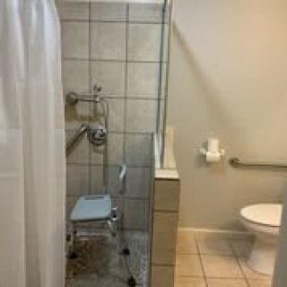A handicap-accessible bathroom featuring a shower with a chair and grab bars, adjacent to a toilet.