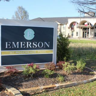 An outdoor sign for Emerson with a building in the background.