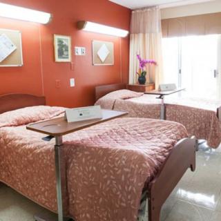 A hospital room with two neatly made beds, featuring a warm color scheme and natural light.