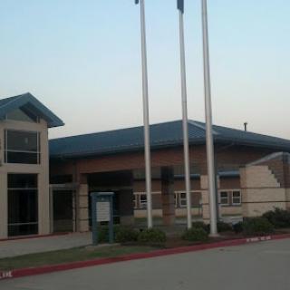 An exterior view of a modern building with flagpoles during sunset.
