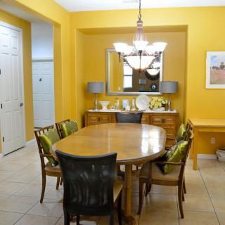 A brightly lit dining room with a wooden table and chairs, featuring yellow walls and a chandelier.