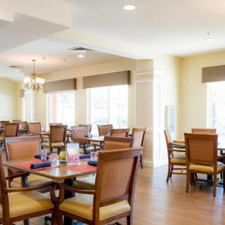 A bright and spacious dining area with neatly arranged tables and chairs, illuminated by natural light from large windows.