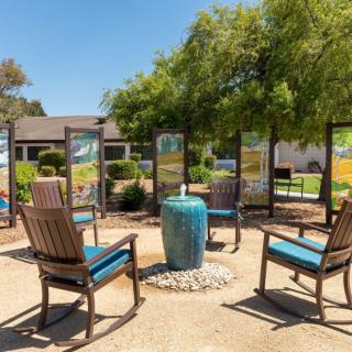 A cozy outdoor seating area with wooden chairs and a small table surrounded by greenery.