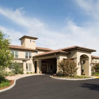 A modern luxury residential building with a spacious driveway under a clear sky.