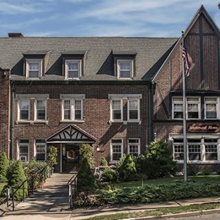 A historic brick building with traditional architecture surrounded by greenery, featuring a flagpole with an American flag.