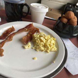 A breakfast plate with bacon and scrambled eggs, accompanied by coffee and muffins.