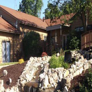 A beautiful house with a landscaped rock garden and surrounding trees basking in the sunshine.