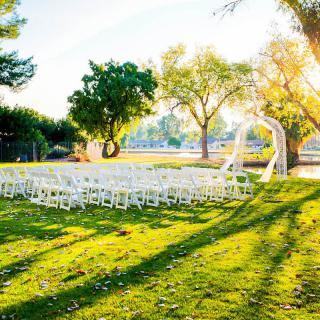 An outdoor wedding setup with rows of white chairs and a ceremonial arch under the trees.