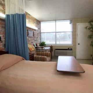 A hospital room with a bed, privacy curtain, and seating area by the window.