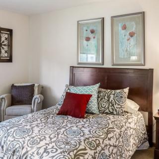 A cozy bedroom with patterned bedding, decorative pillows, and framed artwork on the walls.