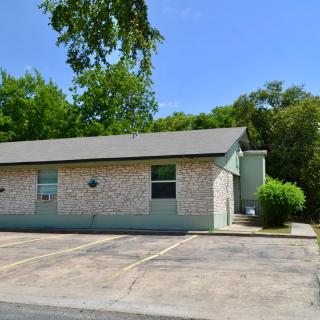 A small office building with a stone exterior and an adjacent parking lot, surrounded by greenery.