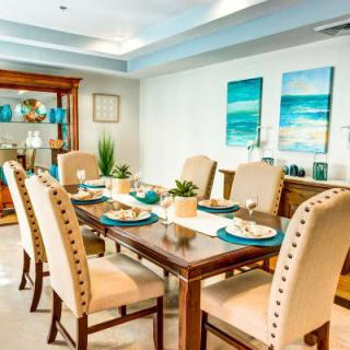 A stylish dining room with a wooden table and upholstered chairs, complemented by nautical-themed artwork.