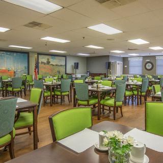 A spacious dining area with green chairs and neatly set tables, illuminated by bright ceiling lights.