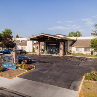 A view of the entrance to a single-story building with a covered driveway and landscaped surroundings under a clear blue sky.