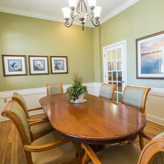A cozy dining room with an oval wooden table, surrounded by upholstered chairs and adorned with wall art.