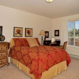 A cozy bedroom with a red and yellow bedspread, wooden furniture, and a window providing natural light.