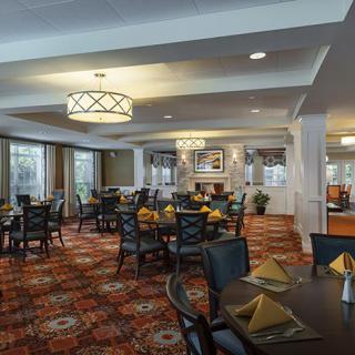 A spacious and elegantly decorated dining room with neatly arranged tables and chairs, featuring warm lighting and a patterned carpet.