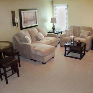 A cozy living room with a sofa, armchair, and coffee table, complemented by a lamp and wall artwork.