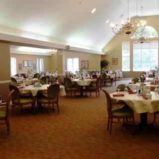 A spacious and elegant dining room with neatly arranged tables and chairs, featuring large windows and chandeliers.