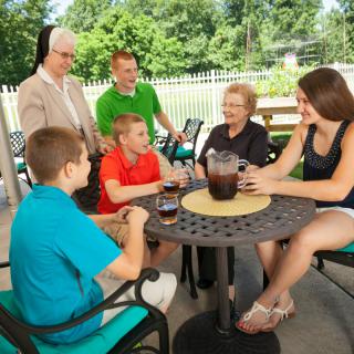 A family enjoying drinks and conversation on a sunny outdoor patio.