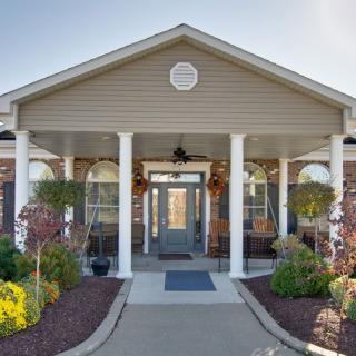 Front view of a building entrance with columns and landscaped surroundings.