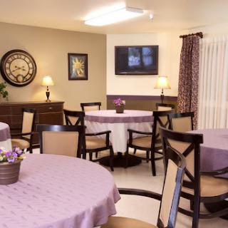 A cozy dining room setup with round tables, comfortable chairs, and a television on the wall.